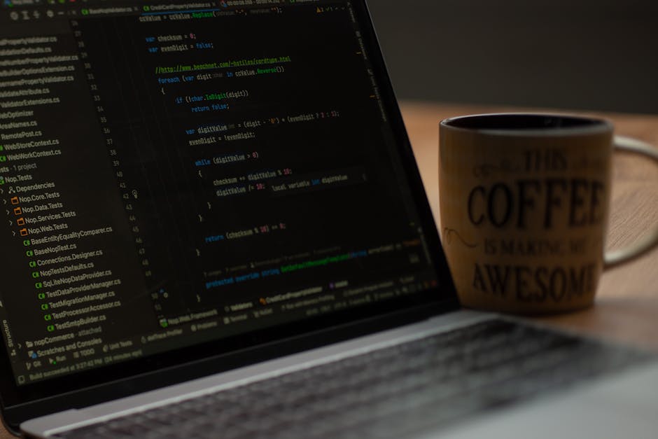 A close-up image of a laptop screen displaying lines of code in a text editor, with visible syntax highlighting in various colors such as green, blue, and yellow. To the right of the laptop, there is