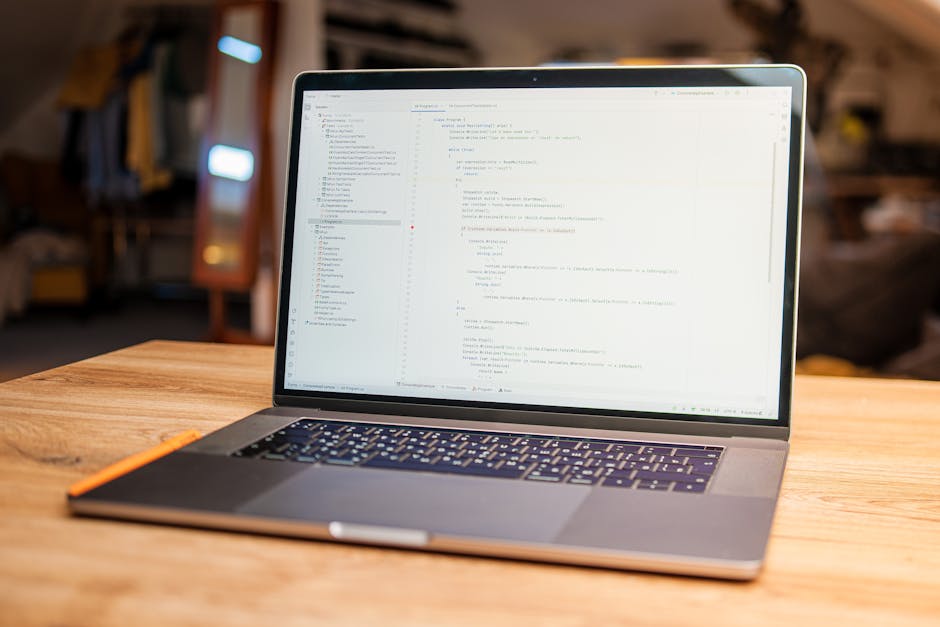 A close-up image of a laptop screen displaying lines of code in a text editor, with visible syntax highlighting in various colors such as green, blue, and yellow. To the right of the laptop, there is